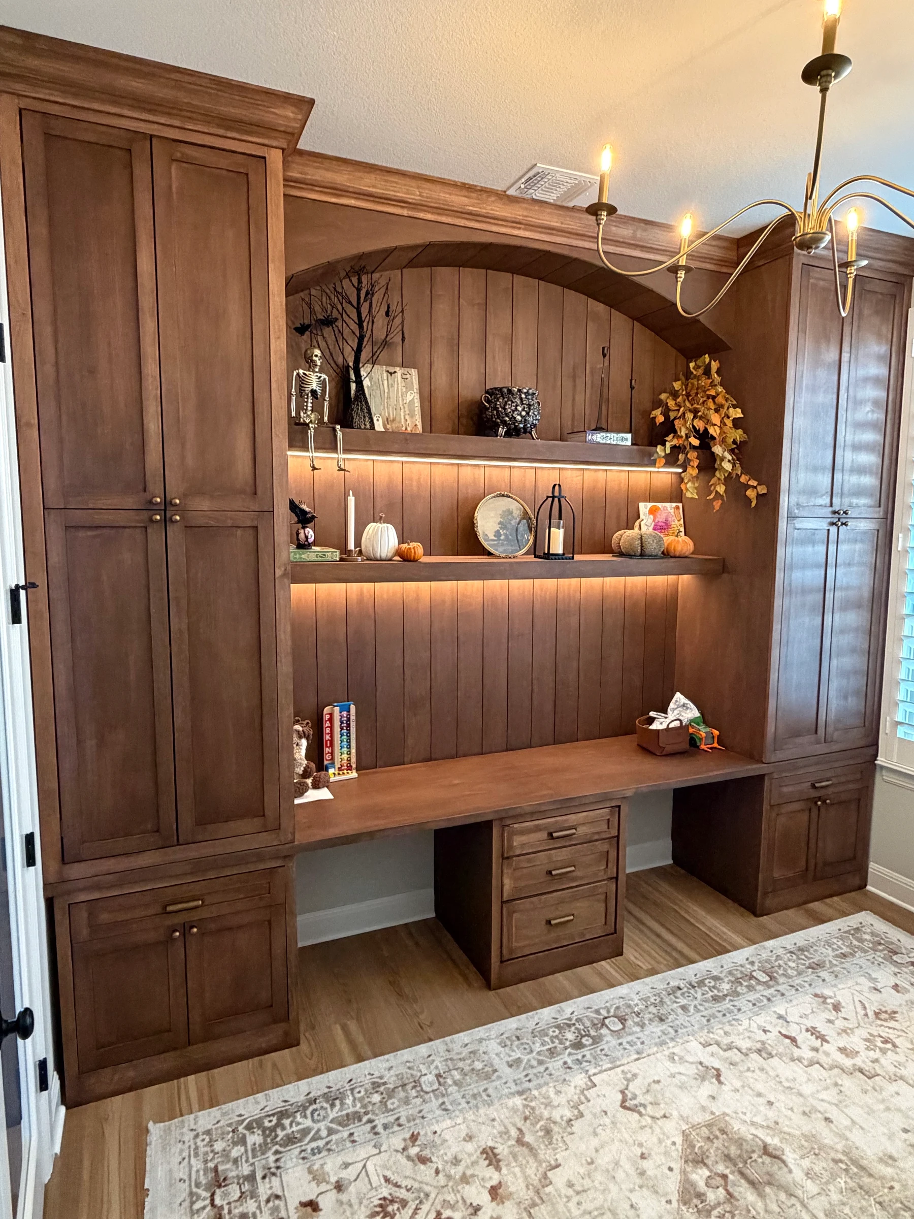 Completed study room built-in with an arched wood surround, lit shelves, desk, and tall cabinets